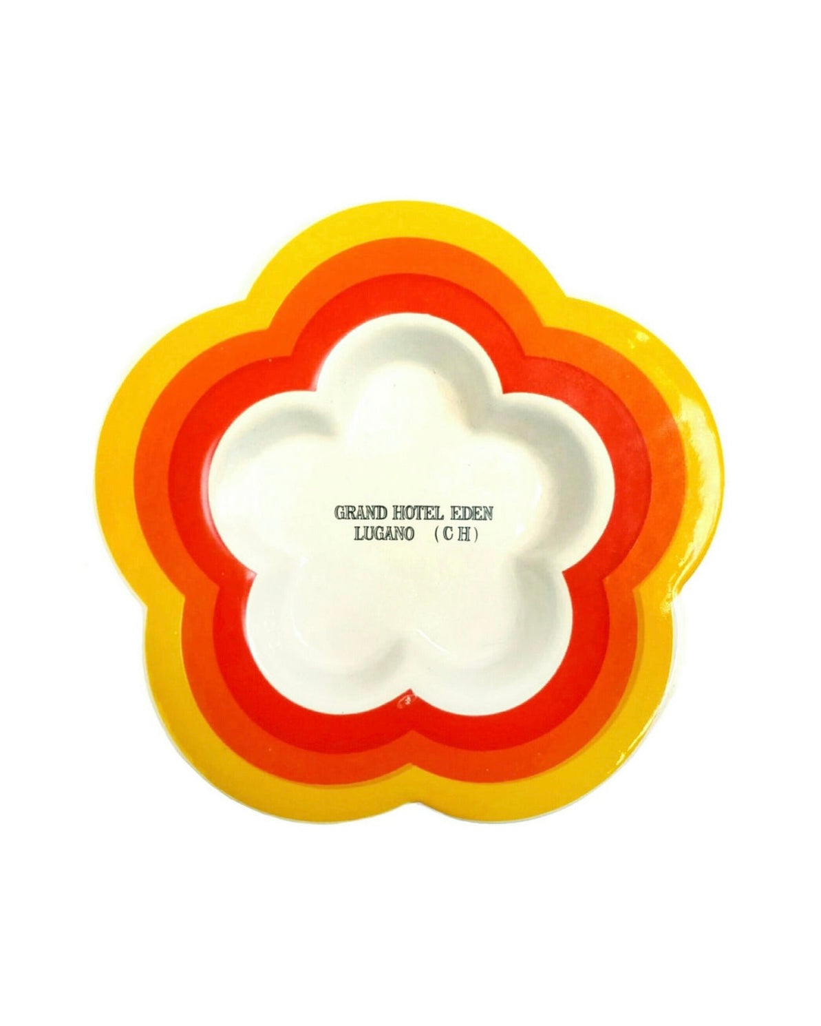 A retro-style ceramic flower-shaped dish with concentric rings of yellow, orange, and red around a white center, featuring the text 'GRAND HOTEL KENEN LUGANO (CH)' printed in the middle.