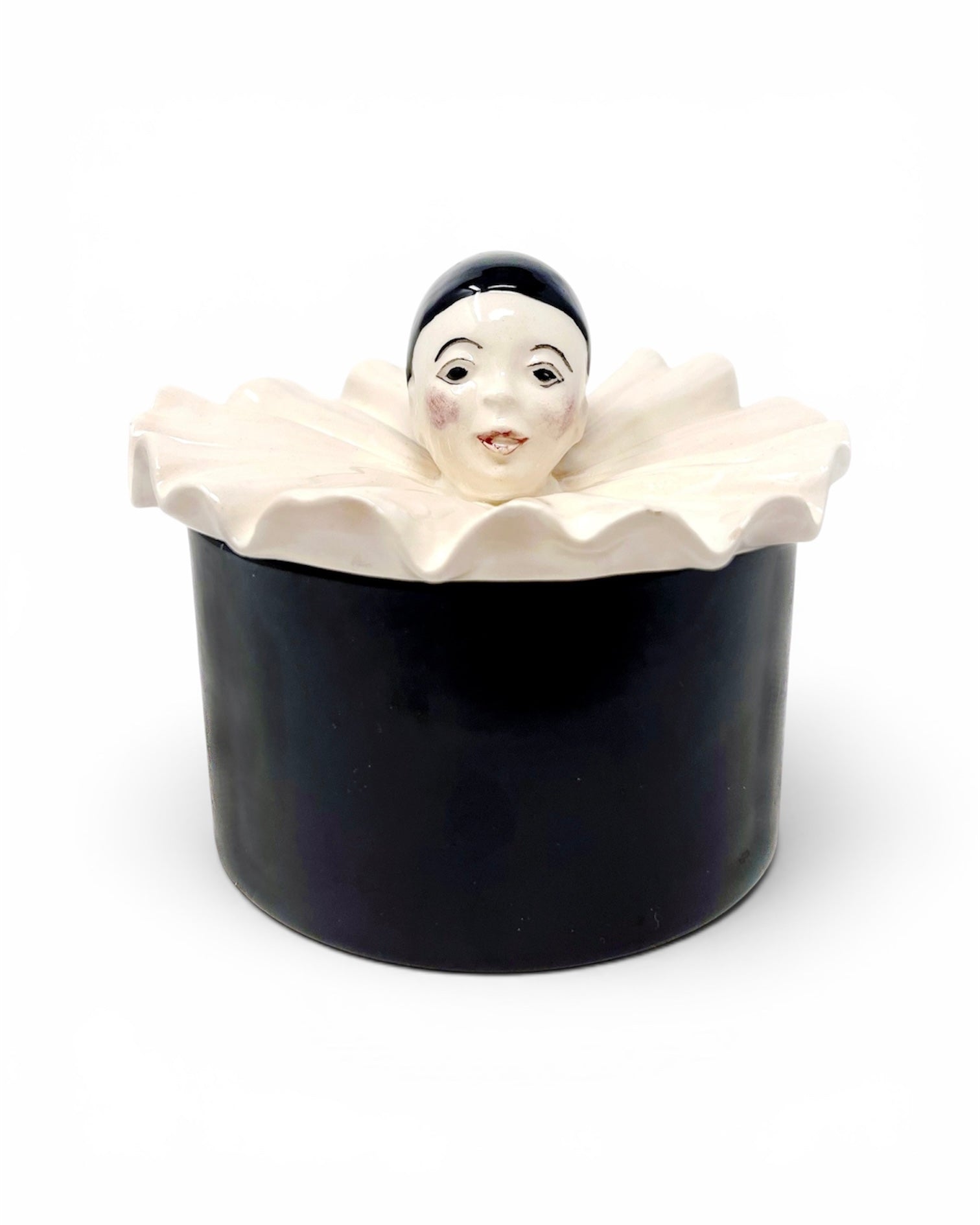 A black ceramic container with a lid shaped like a white ruffled collar, featuring a small sculpted face with black hair peeking out above the rim, photographed on a white background.