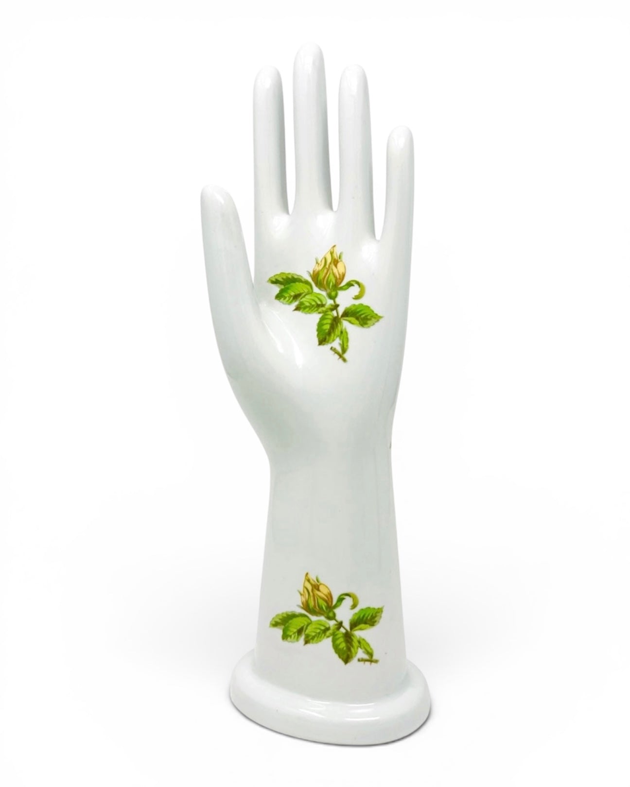 A white ceramic hand-shaped display stand with two green floral motifs, photographed against a seamless white background.